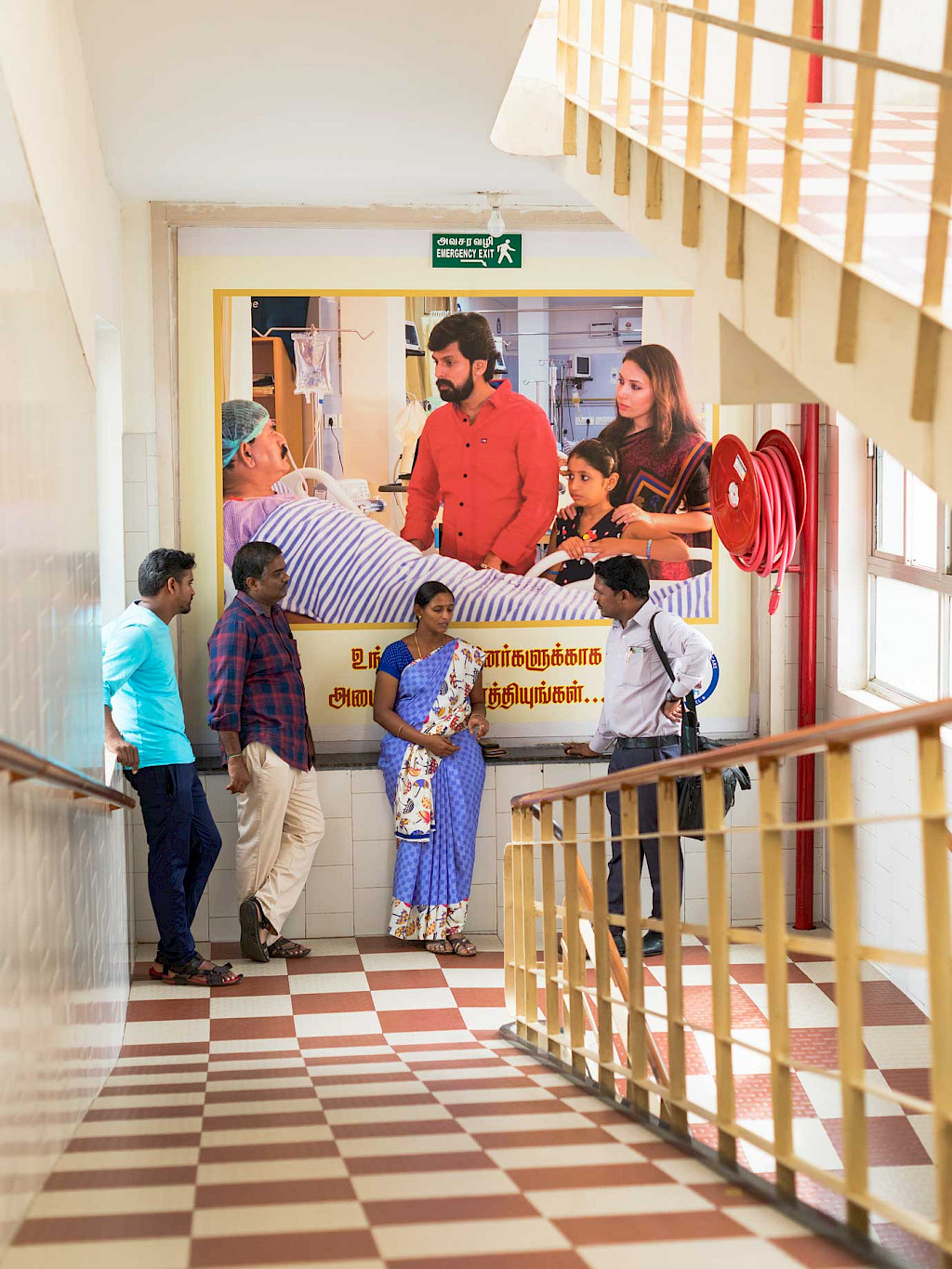 A group of relatives talking to a doctor in the stairwell of the hospital, on the wall behind the group is a large picture of a patient receiving a visit