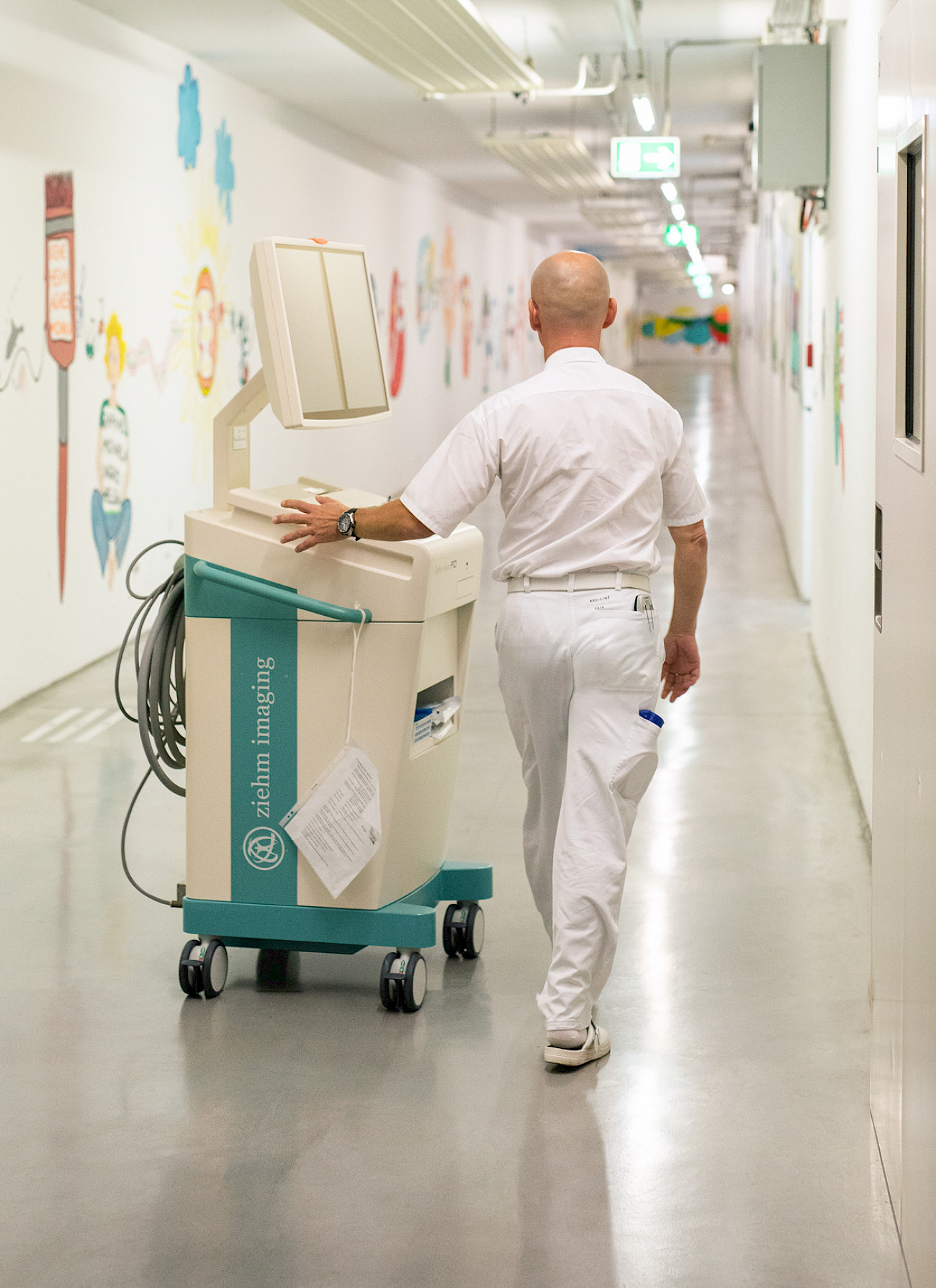 Norbert Lechner, engineer, pushes a Ziehm Imaging monitor cart through a corridor at Kepler University Hospital in Linz.