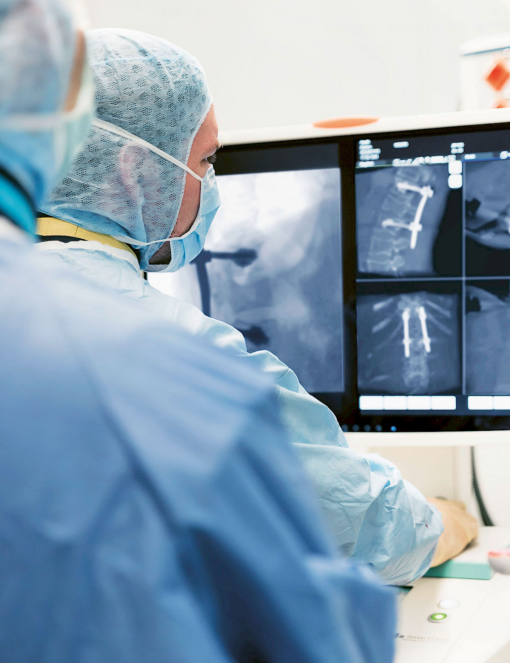 Overshoulder view on a screen: two operating physicians check the exact positioning of various screws.