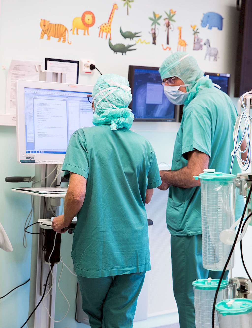 Nursing staff are standing in a hospital corridor, operating a screen on a monitor trolley.