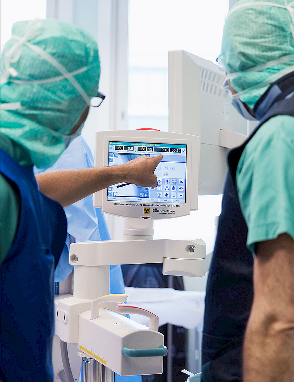 Two members of the surgical team stand in front of a small monitor displaying the user interface for controlling a C-arm.