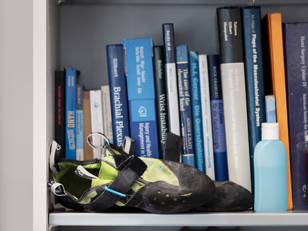 Books on hand surgery share the shelf with climbing shoes and a chalk bag.